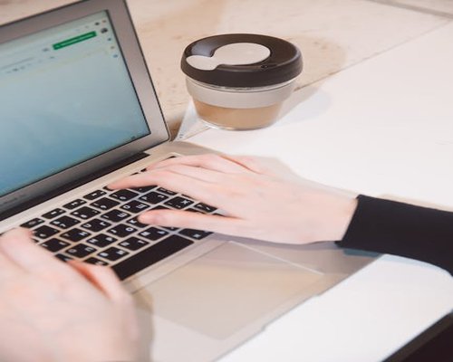 A person typing on a laptop with a cup of coffee nearby
